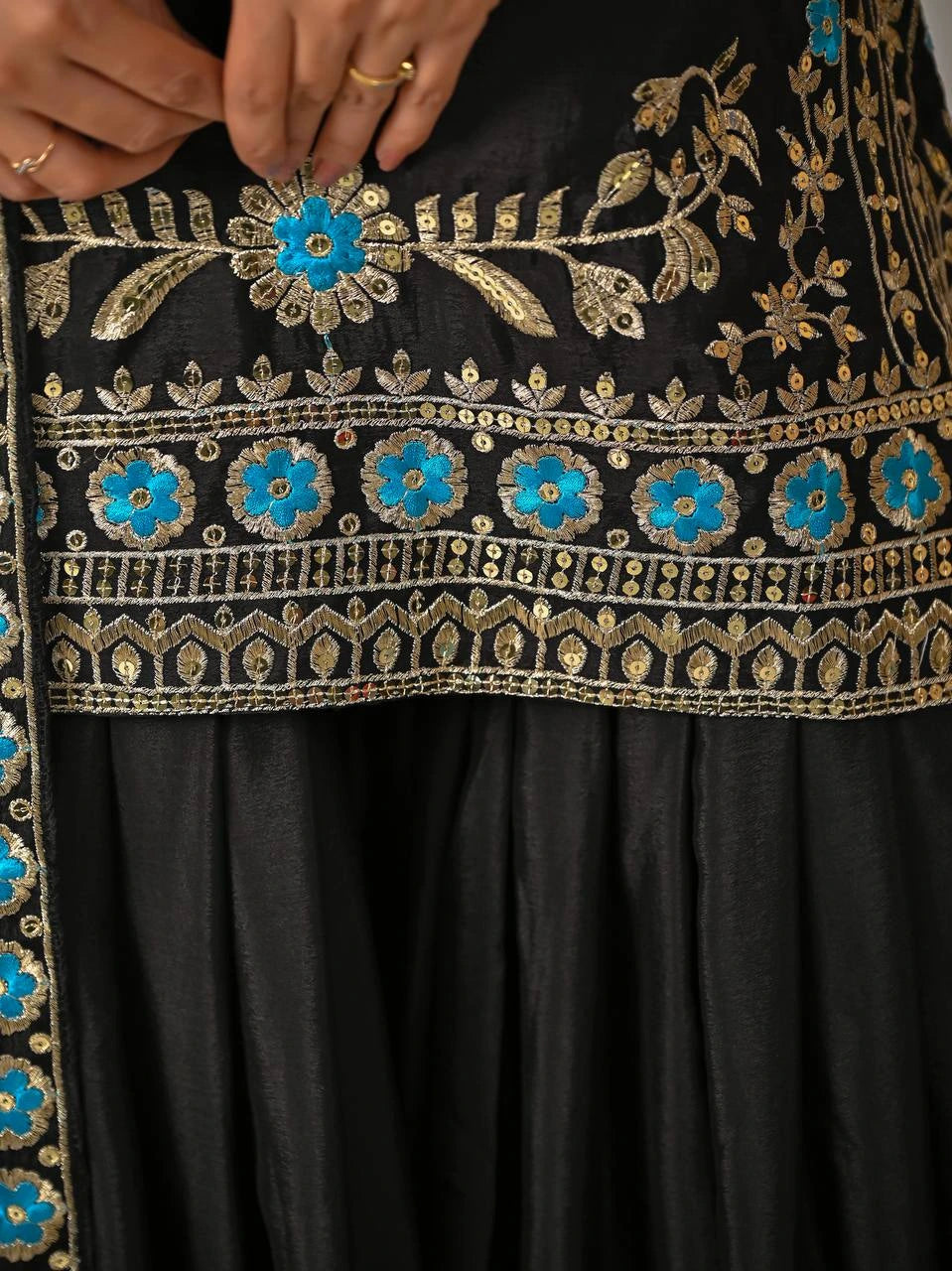 Close-up of a black garment with intricate gold and blue embroidery.